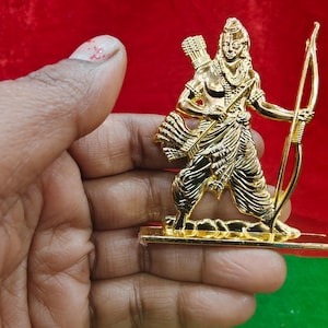 Könnte beinhalten: Goldfarbene Figur einer Gottheit mit Pfeil und Bogen. Die Figur steht auf einem rechteckigen Sockel. Der Hintergrund ist rot und grün.
