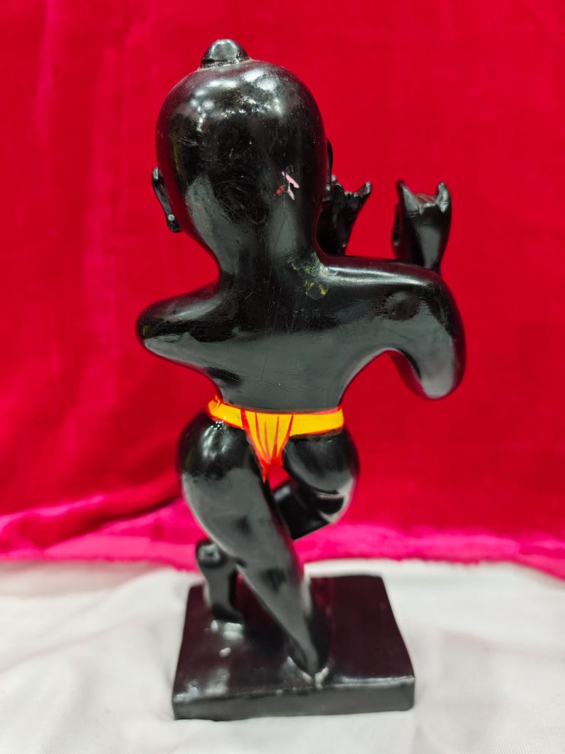 Pu&ograve; includere: Una statuetta nera di una persona in ginocchio, con un indumento giallo e rosso intorno alla vita. La statuetta &egrave; su una base rettangolare nera, con uno sfondo rosso.