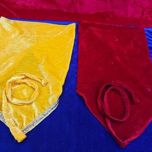 May include: Two velvet bags, one yellow and one red, are displayed against a blue background. The yellow bag has a silver trim and a twisted cord. The red bag has a matching cord. Both bags are rectangular with a pointed bottom.