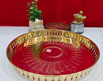 Puede incluir: Una bandeja redonda de metal dorado con interior rojo. La bandeja tiene un diseño floral decorativo y un borde perforado. El número "12" es visible en una pequeña pegatina en el centro. Pequeñas plantas en macetas en el fondo.