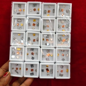 May include: A grid of small, white square display boxes, each holding metallic geometric shapes in silver, gold, and copper hues. The boxes are arranged against a red background. The shapes are various sizes and shapes.