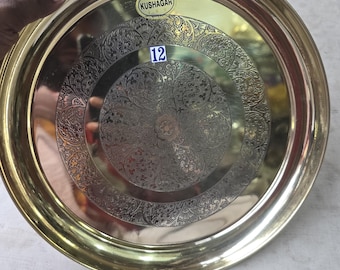 Puede incluir: Una bandeja redonda de metal dorado con un diseño floral grabado en el centro. La bandeja tiene un borde elevado y una pegatina que dice "KUSHAGAR". El número "12" está impreso en una pegatina azul.