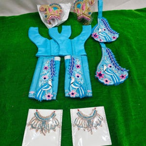 May include: A set of turquoise garments and accessories, including a bodice, skirt pieces, and decorative headpieces. The pieces are adorned with floral and bird embroidery in pink, white, and blue. Two necklaces with blue and pink beads are also included.
