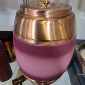 May include: A copper-colored jar with a lid and a small gold knob. The jar has a pink, frosted glass base that fades to white. The lid and top section of the jar are copper-colored.