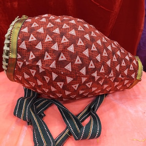 May include: A red and white patterned bag with a green and white strap. The bag features a geometric triangle pattern and is trimmed with gold and green fabric. The strap is green with white and yellow stripes.