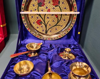 May include: A gold-toned metal serving set with a floral design, presented in a blue velvet-lined box. The set includes a tray, bowls, and a bell. The tray features red and gold floral patterns. The set is designed for serving.