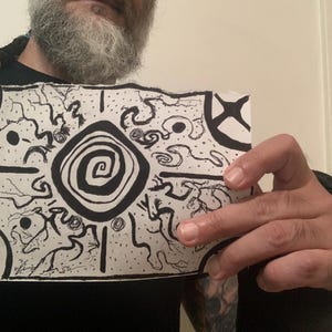 May include: A black and white drawing featuring a central spiral design, surrounded by abstract shapes and lines. The artwork is held up, showcasing the intricate details of the illustration. The overall theme is artistic and graphic.