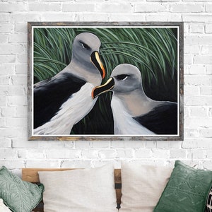 May include: A framed painting of two albatrosses with gray and black feathers, set against a backdrop of green grass. The birds are in a close embrace, with their beaks touching. The artwork is displayed on a white brick wall.