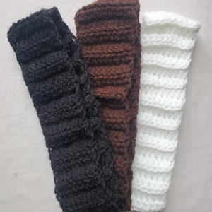 May include: Three crocheted arm warmers in black, brown, and white. Each arm warmer is a solid color and has a ribbed texture. The arm warmers are made of a soft, possibly wool, yarn.