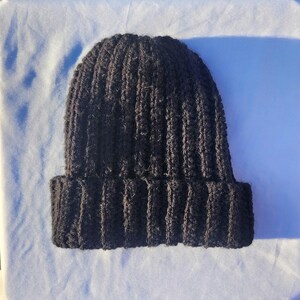 May include: A dark brown, ribbed knit beanie hat. The hat has a folded brim and a close-fitting design. The material appears to be a thick, warm yarn, suitable for cold weather. The hat is a solid color and has a simple, classic style.