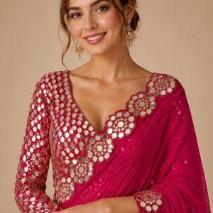 May include: A vibrant fuchsia saree with intricate mirror work detailing. The long-sleeved blouse features a deep V-neckline and is adorned with small, round mirrors. The saree's border and sleeves are embellished with the same reflective accents.