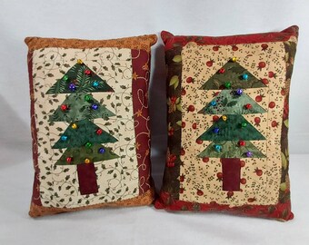 May include: Two quilted pillow covers with a Christmas tree design. The trees are made of green fabric and have red, green, and blue beads for ornaments. The pillows are brown and red with a white background.
