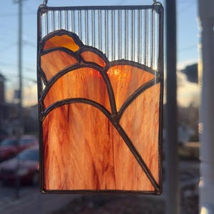 May include: A rectangular stained glass suncatcher featuring a landscape of rolling hills in shades of orange, amber, and red. The upper section consists of clear, vertically ribbed glass, while the lower section uses textured, marbled glass.