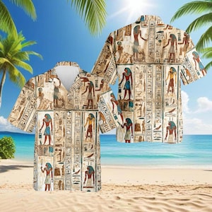May include: Two short-sleeved button-down shirts with an Egyptian hieroglyphic design. The shirts feature a beige background with colorful figures and hieroglyphs. The shirts are displayed on a beach with palm trees and a blue sky.