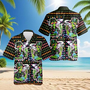 Könnte beinhalten: Schwarzes Hawaiihemd mit einem sich wiederholenden Muster eines grünen Aliens, das eine Bong raucht. Der Außerirdische trägt eine Sonnenbrille und einen Fischerhut. Das Hemd ist mit Cannabispflanzen und bunten Akzenten verziert. Der Hintergrund zeigt eine Strandszene.