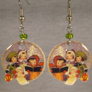 May include: A pair of dangle earrings featuring a winter scene with children singing carols. The round pendants have a scalloped edge and are adorned with a green bead. The earrings are silver-toned and have a hook closure.
