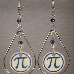 May include: A pair of silver-toned dangle earrings. Each earring features a teardrop-shaped frame with a circular charm displaying the mathematical symbol Pi in blue on a white background. Blue and clear beads add detail.