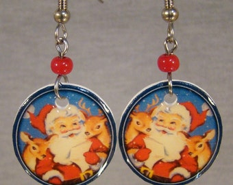 May include: A pair of Christmas-themed earrings. Each earring features a circular pendant with a blue background and a vintage illustration of Santa Claus and two reindeer. Red beads and silver-tone metal hardware complete the design.