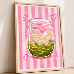 Puede incluir: Una lámina de arte enmarcada que muestra un vaso sin tallo lleno de líquido con remolinos rosas y verdes. El fondo consiste en rayas verticales rosas y blancas, acentuado con formas de corazón dibujadas a mano y pequeñas líneas radiantes.