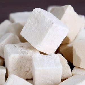May include: Close-up of a pile of white, cube-shaped food items. The cubes have a slightly rough texture and vary in size. The lighting highlights the edges and surfaces of the cubes, creating shadows and depth. The overall color palette is neutral, with shades of white and off-white.