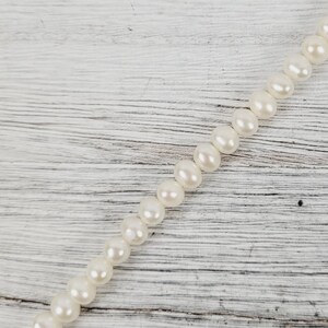 May include: A strand of white pearls on a white wooden surface.