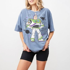 Puede incluir: Camiseta azul claro con un dise&ntilde;o de Buzz Lightyear. El dise&ntilde;o muestra a Buzz con su traje espacial, un cohete, estrellas y el texto "BUZZ LIGHTYEAR". La camiseta se combina con unos pantalones cortos negros.