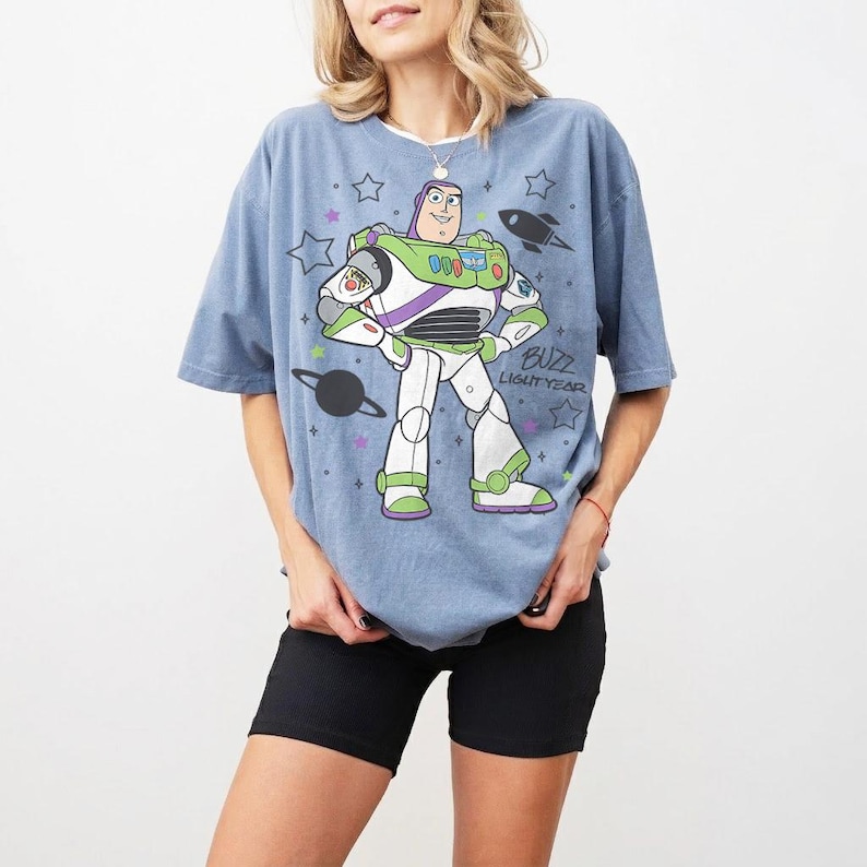 Puede incluir: Camiseta azul claro con un dise&ntilde;o de Buzz Lightyear. El dise&ntilde;o muestra a Buzz con su traje espacial, un cohete, estrellas y el texto "BUZZ LIGHTYEAR". La camiseta se combina con unos pantalones cortos negros.