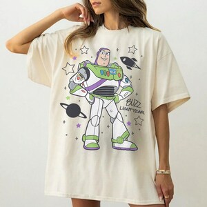 Puede incluir: Camiseta color crema con un dise&ntilde;o de Buzz Lightyear de Toy Story. El dise&ntilde;o incluye a Buzz con su traje espacial, estrellas, un cohete y el texto "Buzz Lightyear". La camiseta tiene mangas cortas y un corte holgado.