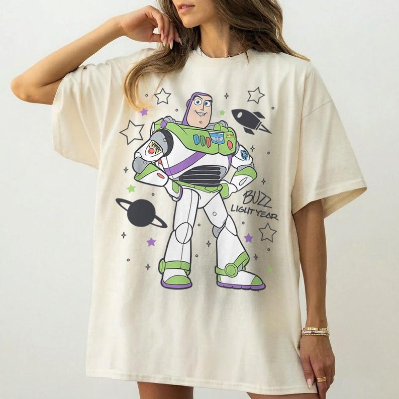 Puede incluir: Camiseta color crema con un dise&ntilde;o de Buzz Lightyear de Toy Story. El dise&ntilde;o incluye a Buzz con su traje espacial, estrellas, un cohete y el texto "Buzz Lightyear". La camiseta tiene mangas cortas y un corte holgado.