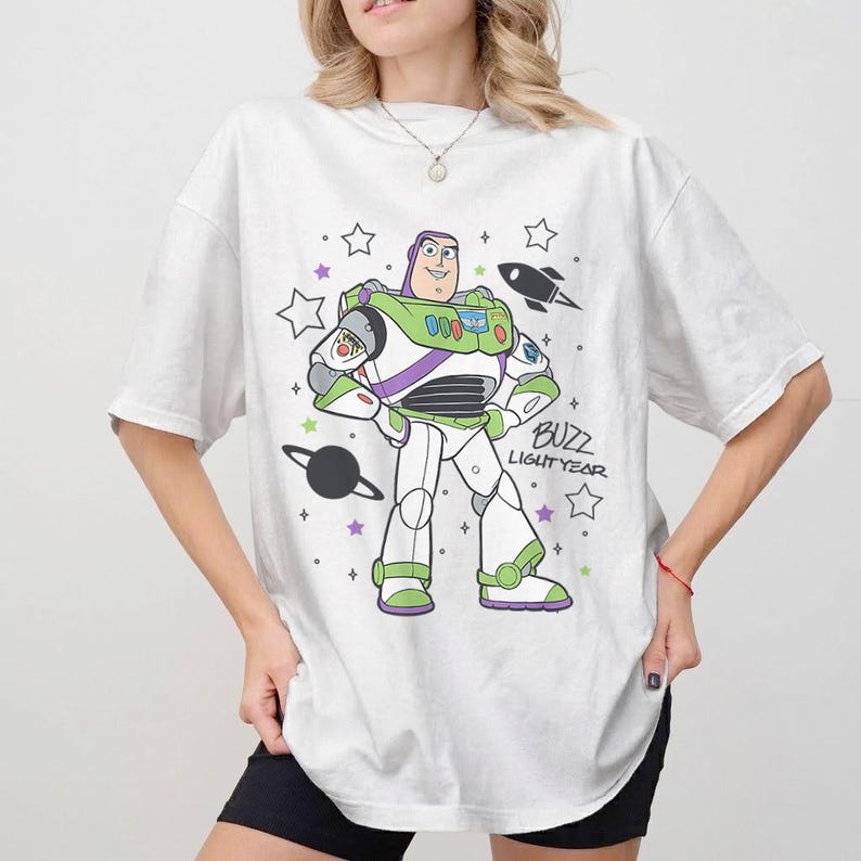 Puede incluir: Camiseta blanca con un gr&aacute;fico de dibujos animados de Buzz Lightyear. El dise&ntilde;o incluye a Buzz con su traje espacial, un cohete, estrellas y las palabras "Buzz Lightyear". La camiseta tiene mangas cortas y un corte holgado.