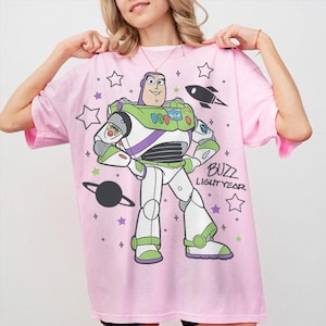 Puede incluir: Camiseta rosa claro con un dise&ntilde;o de Buzz Lightyear de Toy Story. El dise&ntilde;o incluye a Buzz, estrellas, un cohete y el texto "Buzz Lightyear". La camiseta es de color rosa claro.