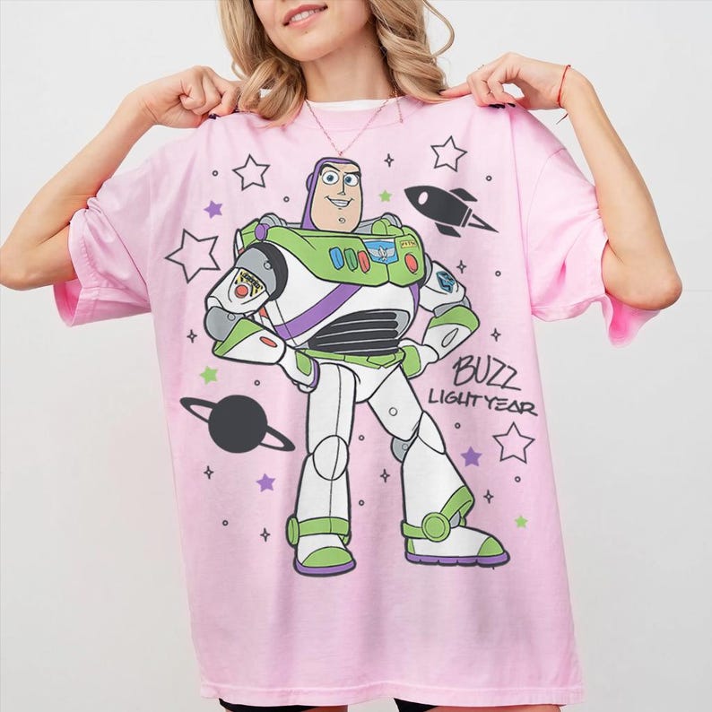 Puede incluir: Camiseta rosa claro con un dise&ntilde;o de Buzz Lightyear de Toy Story. El dise&ntilde;o incluye a Buzz, estrellas, un cohete y el texto "Buzz Lightyear". La camiseta es de color rosa claro.