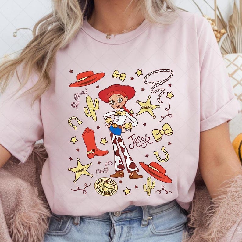 Peut inclure: T-shirt rose clair avec une illustration de dessin anim&eacute; de Jessie de Toy Story. Le design comprend un chapeau rouge, des bottes et le nom "Jessie". Des &eacute;l&eacute;ments suppl&eacute;mentaires incluent des &eacute;toiles, un lasso et un badge de sh&eacute;rif.