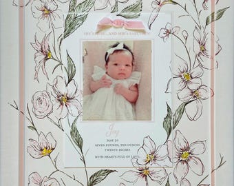 May include: A white frame with a pink border and floral design. A photo of a baby girl is in the center of the frame. The text "SHE'S HERE AND SHE'S FABULOUS" is above the photo. The text "Joy" is below the photo, followed by "MAY 30", "SEVEN POUNDS, TEN OUNCES", "TWENTY INCHES", and "WITH HEARTS FULL OF LOVE."