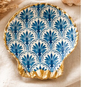 May include: A seashell-shaped decorative plate with a gold rim and a blue and white floral pattern. The plate has a scalloped edge and is likely made of ceramic or porcelain.