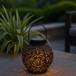 May include: A black, spherical solar lantern with a floral pattern. The lantern has a handle and emits a warm glow. The cut-out design creates light patterns. The lantern is suitable for outdoor use and is made of metal.