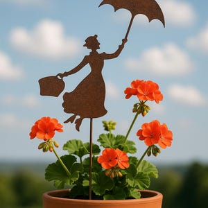 Puede incluir: Silueta metálica de una mujer con paraguas y bolso, colocada en una maceta de terracota con geranios de color naranja brillante. El fondo muestra un cielo azul con nubes blancas.