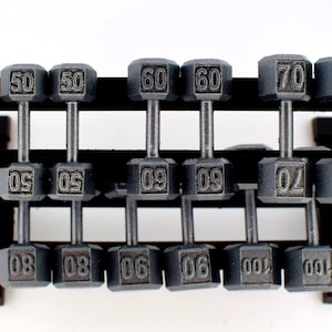 K&ouml;nnte beinhalten: Graue Kurzhanteln, von 22.68 kg bis 45.36 kg, auf einem schwarzen Rack. Jedes Gewicht ist deutlich beschriftet und bietet eine Auswahl an Gr&ouml;&szlig;en f&uuml;r ein umfassendes Training. Das Rack ist stabil und gut organisiert.