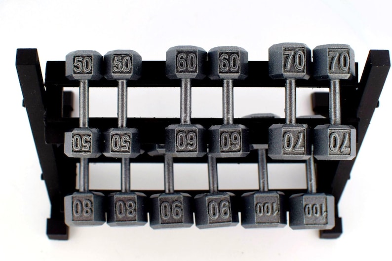 K&ouml;nnte beinhalten: Graue Kurzhanteln, von 22.68 kg bis 45.36 kg, auf einem schwarzen Rack. Jedes Gewicht ist deutlich beschriftet und bietet eine Auswahl an Gr&ouml;&szlig;en f&uuml;r ein umfassendes Training. Das Rack ist stabil und gut organisiert.