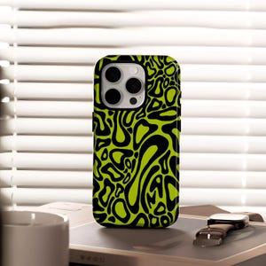May include: A black and neon green phone case with an abstract design. The case is on a book with a watch beside it. The phone case has a camera cutout and buttons.