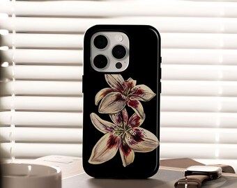 May include: Black phone case featuring a watercolor illustration of two lilies. The flowers have white petals with maroon and yellow accents. The case is shown on a book with a watch.