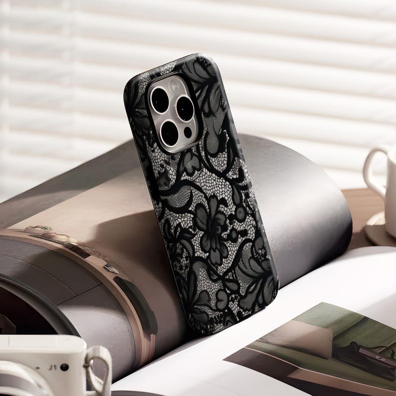 May include: Black phone case with a delicate lace pattern. The case features a floral design with intricate details, offering a stylish and protective accessory. The case is designed to fit a smartphone.