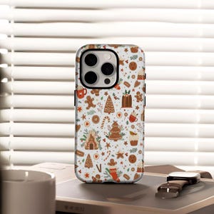 Puede incluir: Una funda de teléfono blanca con un tema festivo de pan de jengibre. La funda presenta un patrón repetido de hombres de jengibre, árboles de Navidad, casas y otros elementos temáticos navideños en marrón, rojo y verde.