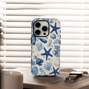 Puede incluir: Una funda de teléfono con un patrón repetido de estrellas de mar azules, conchas marinas y algas marinas sobre un fondo crema. La funda tiene un borde negro y un recorte para la cámara. El diseño evoca un tema costero o náutico.