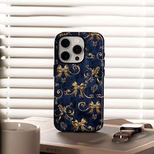 May include: A navy blue phone case with a gold bow and floral pattern. The case has a glossy finish and a camera cutout. The design features multiple gold bows and swirling floral elements against a dark blue background. The case is on a book with a watch.