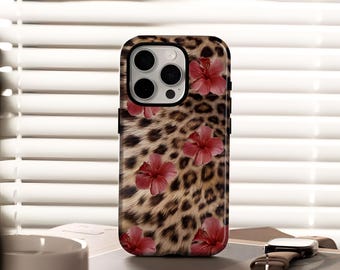 May include: A phone case featuring a leopard print design with red hibiscus flowers. The case has a black border and is designed for a smartphone. The background is a blurred view of a window with white blinds.