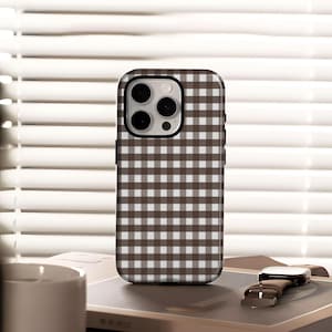 May include: A brown and white checked phone case. The case has a square pattern and a black border. The phone case is on a book with a watch next to it.