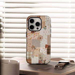 Op de afbeelding: Een telefoonhoesje met een patchwork-ontwerp in bruin-, beige- en crèmetinten, met bloemen-, geruite en effen secties. De hoes heeft een zwarte rand en een camera-uitsparing. Een horloge met een bruine leren band ligt ernaast.