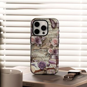 Op de afbeelding: Een telefoonhoesje met een vintage design met rozen, vlinders en muzieknoten. De hoes heeft een bloemige en antieke uitstraling, met een kleurenpalet van paars, roze en crème. Het ontwerp bevat een open boek en parels.