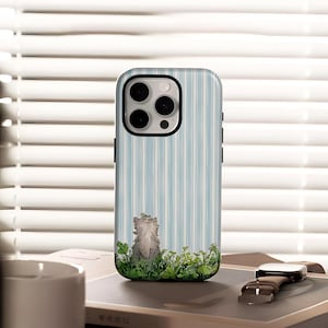May include: A phone case with a light blue and white striped pattern. The case features a cartoon illustration of a gray cat sitting in green foliage. The phone case has a black border and a camera cutout.
